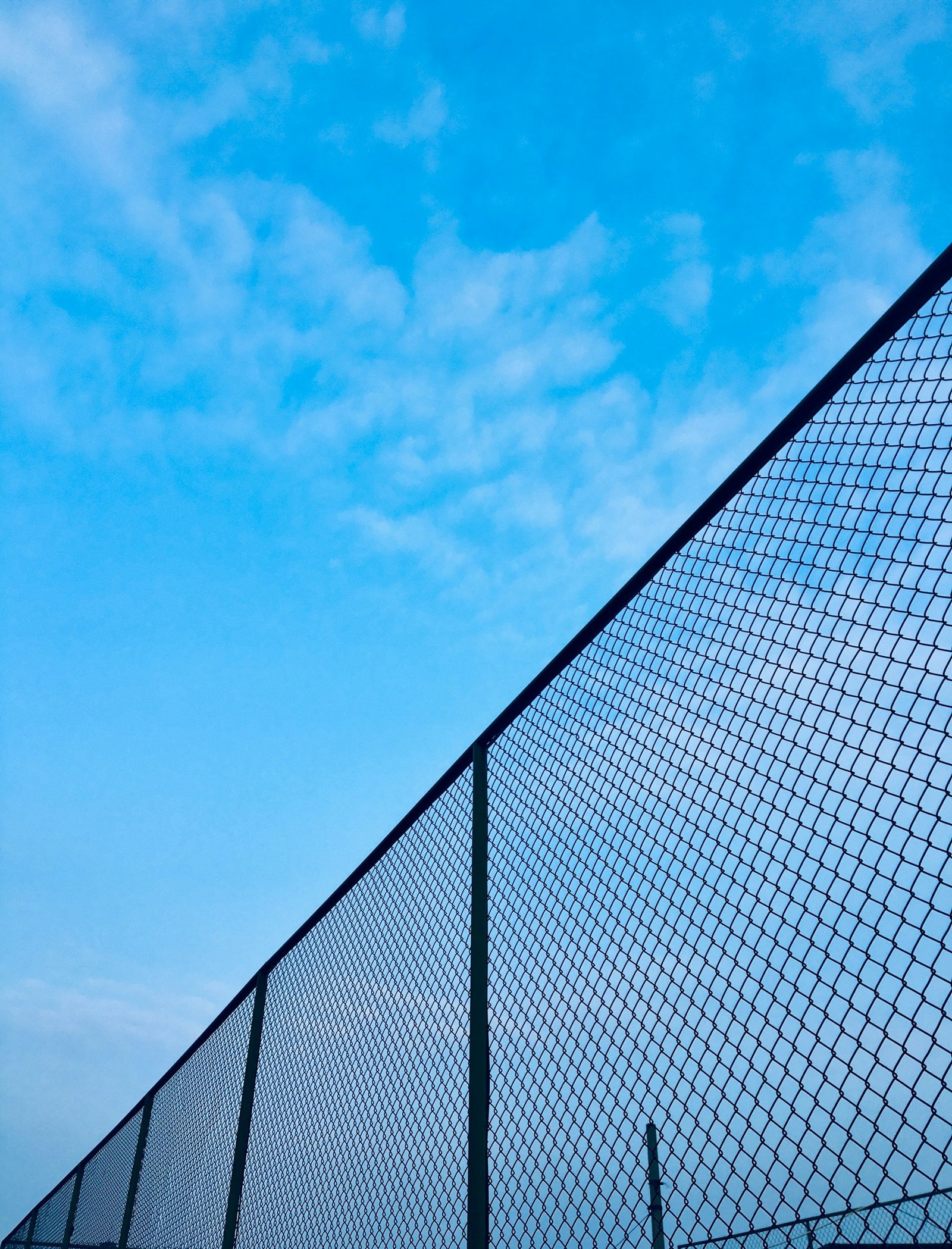 Chain link fence receding into the distance under a bright blue sky