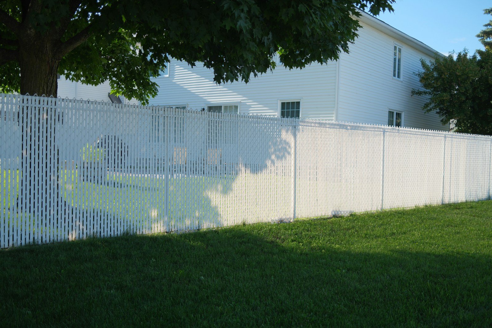 White vinyl privacy fence with a slatted top running along a lawn beside a two-storey house