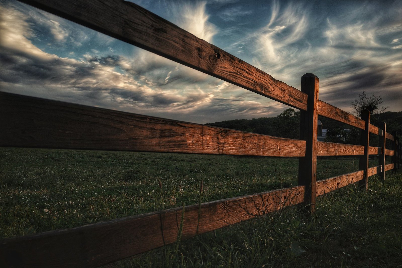 Stained post-and-rail fence running away across a field at dusk