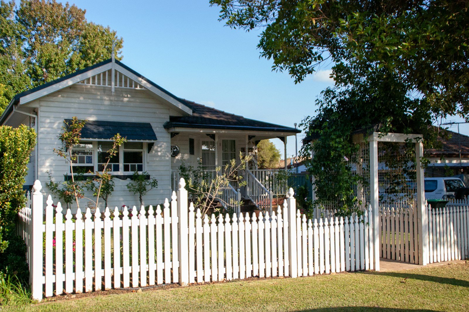 White picket fence with a gate across the front garden of a weatherboard house on a sunny day