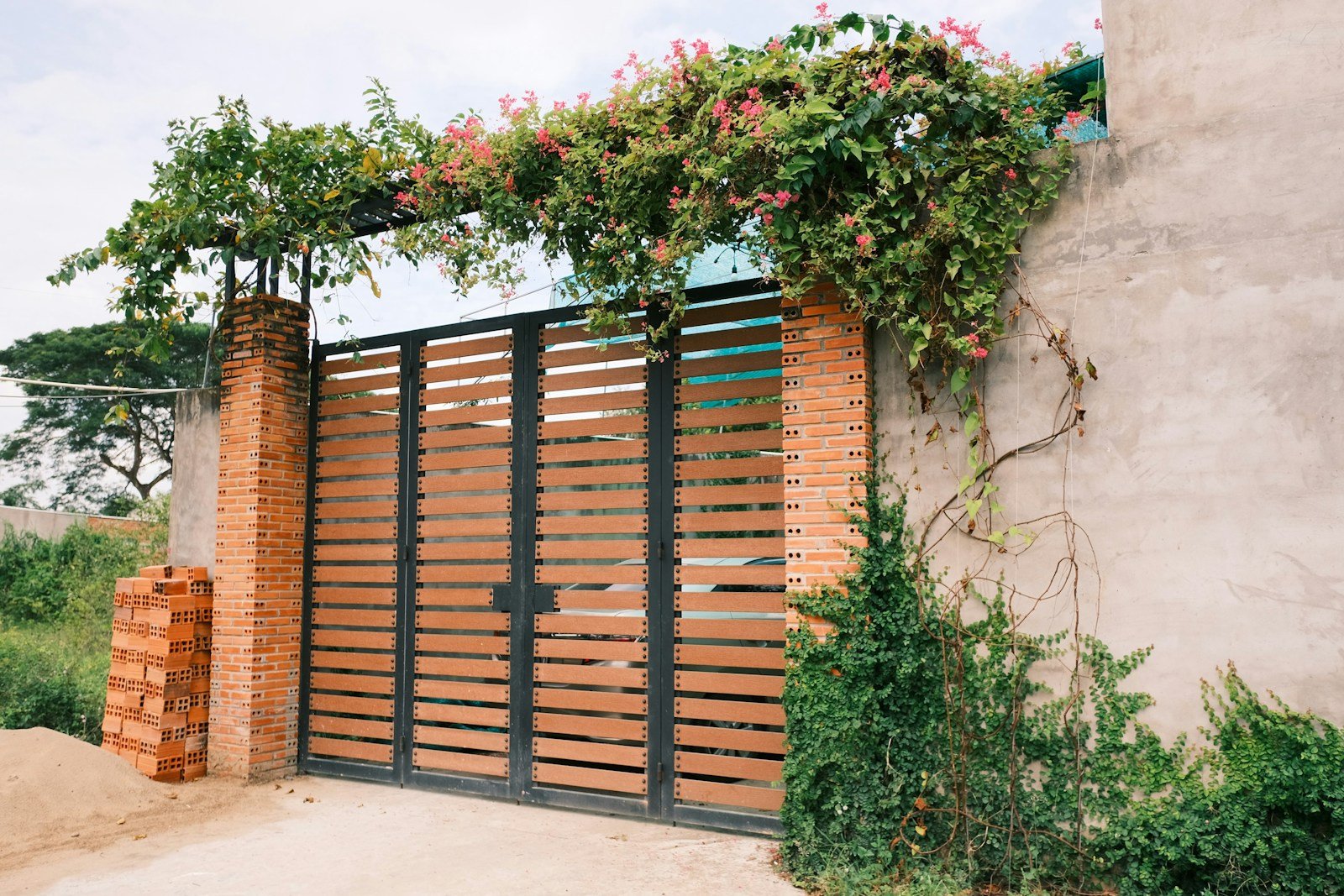 Gate built from horizontal timber slats in a steel frame, with flowering climber growing over the top